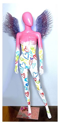 a pink female mannequin with wings and hearts on it's body is standing in front of a wall