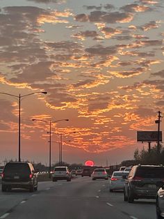 cars are driving down the road as the sun sets in the sky behind them,