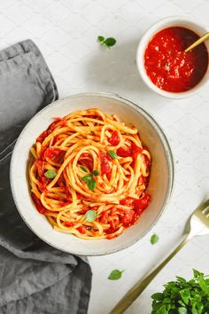 a bowl of spaghetti with sauce and parsley on the side next to a spoon