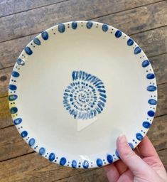 a hand holding a blue and white plate with an image of a snail on it