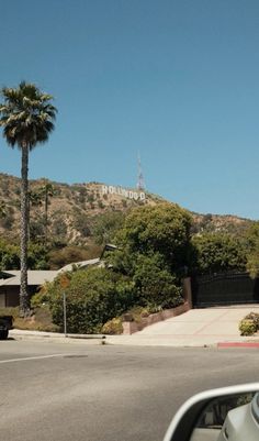 there is a car driving down the street in front of a hill with palm trees