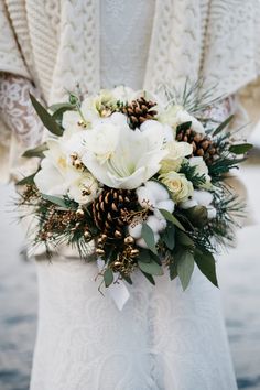 a bridal bouquet with white flowers and pine cones on the bride's dress