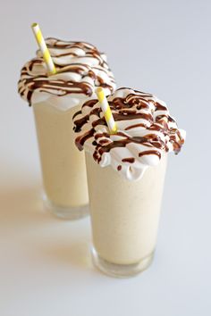 two glasses filled with milkshakes and topped with chocolate drizzled on top