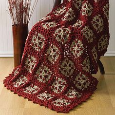 a crocheted blanket sitting on top of a wooden chair next to a vase