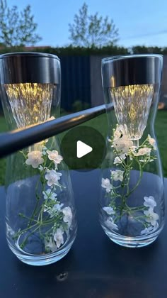 two clear vases with flowers in them sitting on a table next to each other