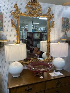 an ornate gold framed mirror sitting on top of a wooden dresser next to two lamps