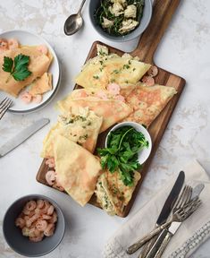 some food is laying out on a wooden cutting board next to silverware and utensils