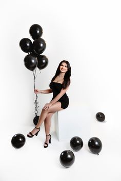 a woman sitting on top of a white box holding black balloons