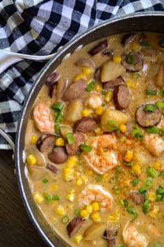 a pot filled with shrimp, potatoes and green onions on top of a wooden table