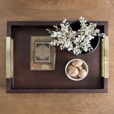 a wooden tray with flowers and a book on the top, next to a bowl of nuts