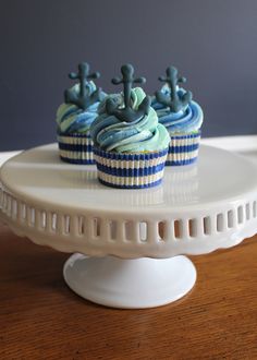 two cupcakes with blue frosting and anchors on top sitting on a cake plate