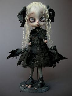 a doll with white hair and blue eyes wearing a black dress is standing in front of a gray background