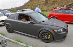 a grey car parked on the side of a road next to other cars and people