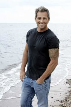 a man standing on top of a sandy beach next to the ocean with his hands in his pockets