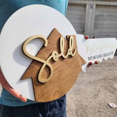 a person holding a wooden sign that says sold