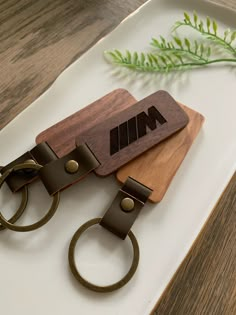 two wooden keychains sitting on top of a white plate next to a green plant