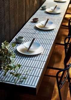 the table is set with four plates and two cups on it, along with plants