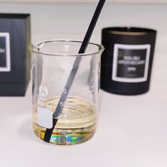 an empty glass with a black straw in it next to a box and two candles