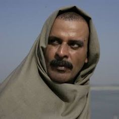 a man wearing a shawl standing in front of the ocean looking at the camera