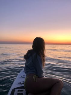 a woman sitting on top of a surfboard in the middle of the ocean at sunset