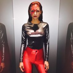 a woman with red hair and makeup is standing in front of two mirrors wearing leather pants