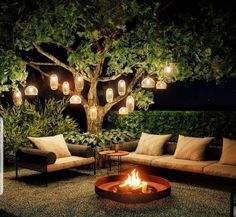 an outdoor fire pit surrounded by furniture and trees with lights hanging from the tree branches