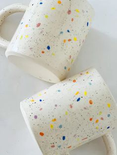 two white coffee mugs with sprinkles on them sitting side by side