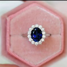 a blue and white diamond ring sitting on top of a pink velvet box