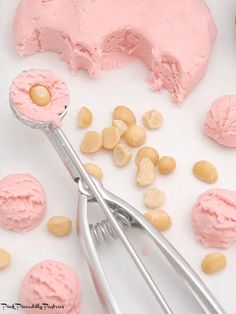 a pink frosted doughnut with nuts and a pair of tongs