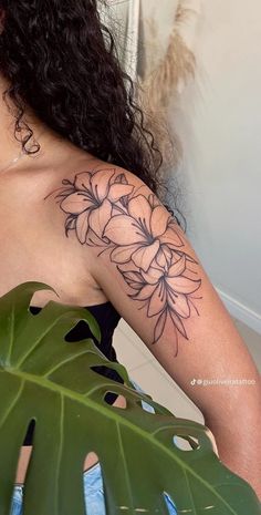 a woman with a flower tattoo on her arm and shoulder, sitting next to a large green leaf