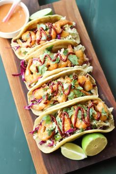 several tacos are lined up on a cutting board with lime wedges and dipping sauce