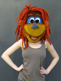 a woman with red hair wearing a brown shirt and grey tank top standing in front of a gray wall