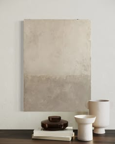 two white vases sitting on top of a wooden table next to a large painting