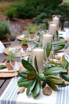 the table is set with candles, plates and greenery on it's placemats