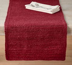 a red table runner on top of a wooden floor next to a white plate and silverware