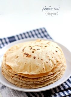 stack of pita bread sitting on top of a white plate next to a blue and white checkered napkin