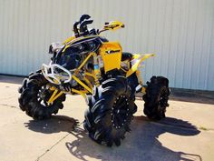 a yellow and black four - wheeler is parked in front of a building with large tires