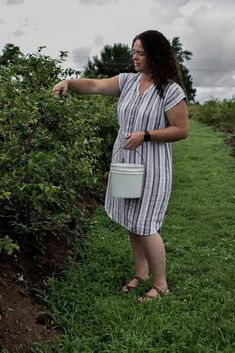 a woman standing in the grass holding a bucket and pointing to something on her hand