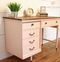 a pink desk with three drawers and a clock on top, next to a potted plant