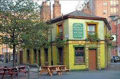 an old building painted yellow and green with flowers on the windows, next to picnic tables