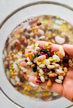 someone holding up their hand full of beans and corn in a bowl with other food items