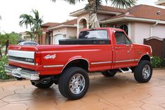 a red pick up truck parked in front of a house with palm trees on the driveway