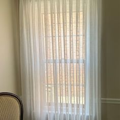 a chair sitting in front of a window with white curtains