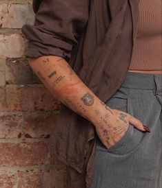 a woman standing next to a brick wall with tattoos on her arm