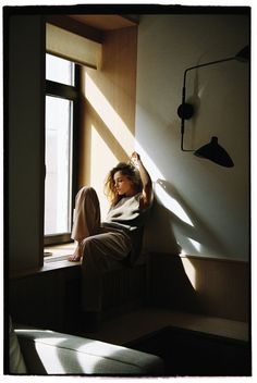 a woman sitting on a window sill in front of a window with the sun shining through