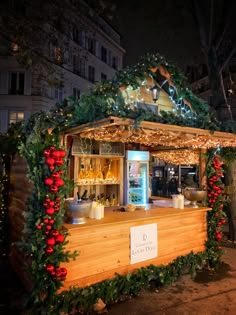 an outdoor bar decorated with greenery and christmas lights at night in front of a building