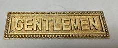 a gold metal name plate with the word gentlemen written in large, ornate letters on it