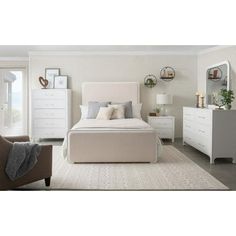 a white bed sitting in a bedroom next to a dresser and chair with pillows on top of it