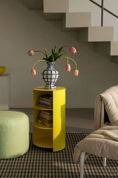 a vase with flowers sitting on top of a yellow shelf next to a chair and ottoman