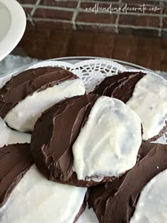 chocolate covered cookies with white frosting on a glass plate next to a brick wall